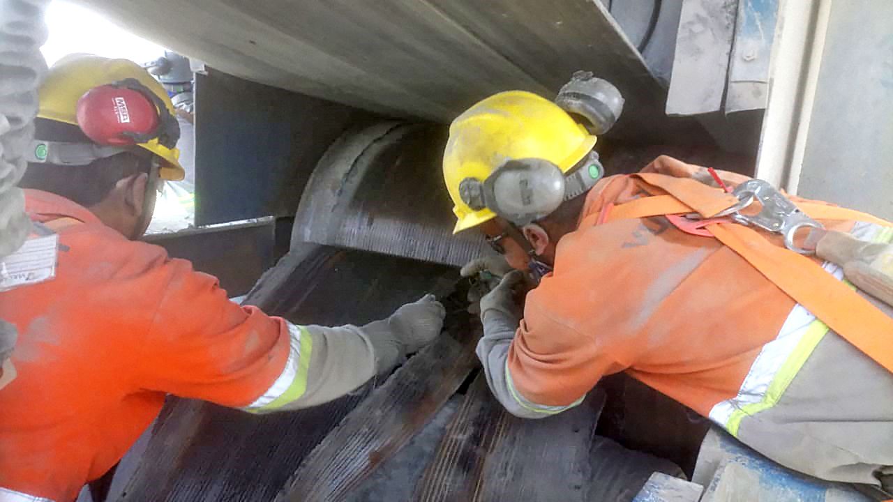 Técnicos com capacete e protetor auricular trabalhando junto a um rolo